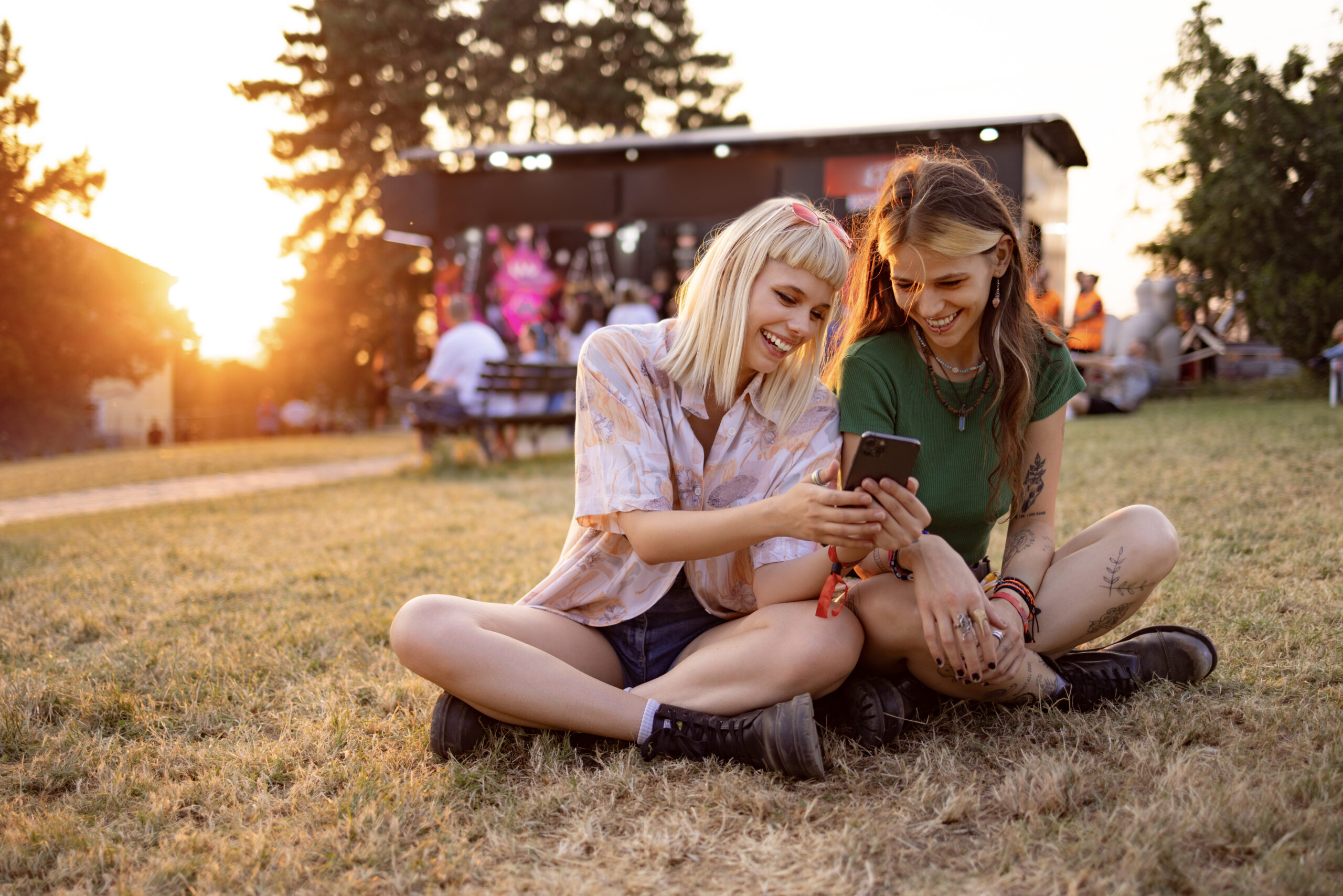 Happy female festival goers using smart phone at sunset.