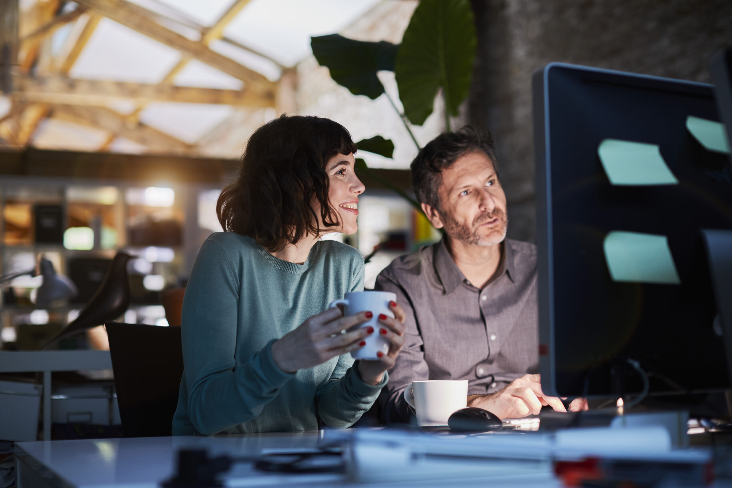 Zwei Personen am Abend im Office sitzen gemeinsam vor dem Computer.