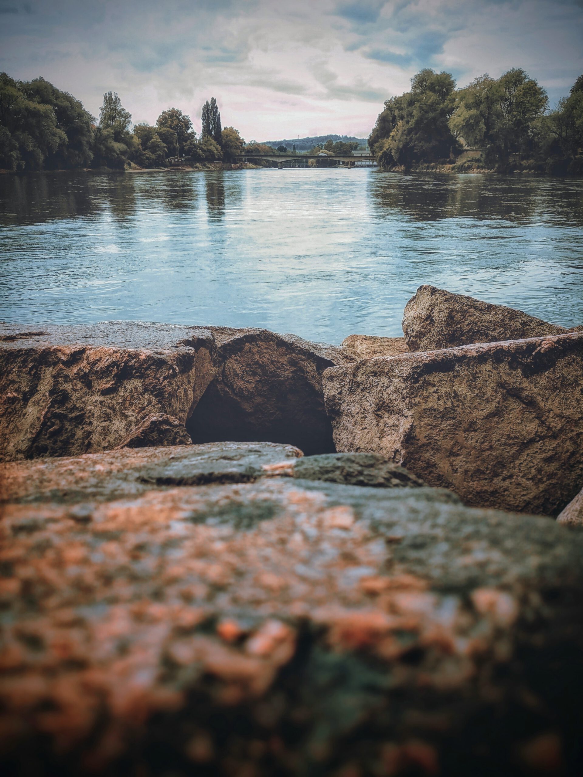 Fluss mit Steinen im Vordergrund und Brücke im Hintergrund