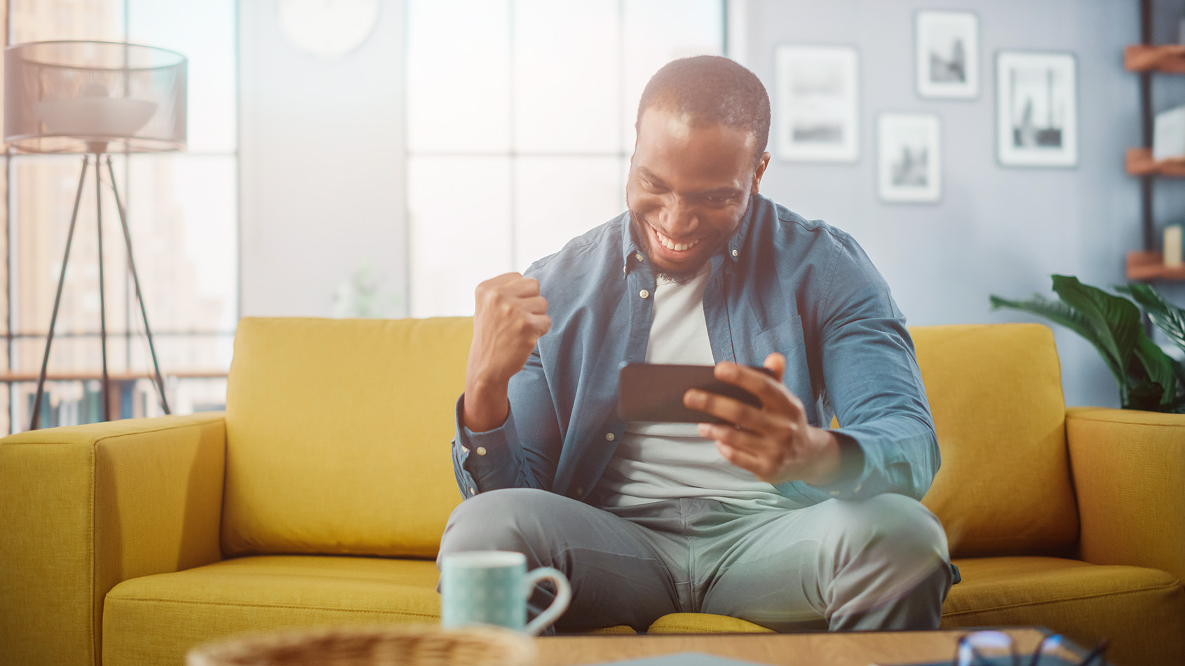 Man sitzt auf einem Sofa schaut aufs Handy und freut sich über etwas, was er dort sieht.