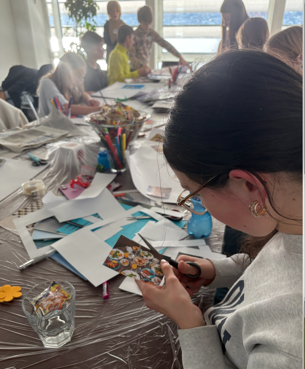 Ein Mädchen schneidet etwas aus an einem grossen Tisch mit bastelnden Kindern.