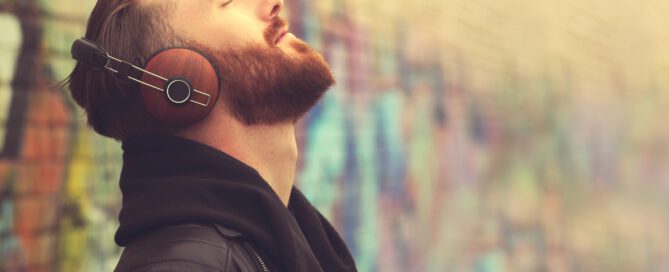 Mann mit Kopfhörern steht an Wand mit Graffiti und hört Audio