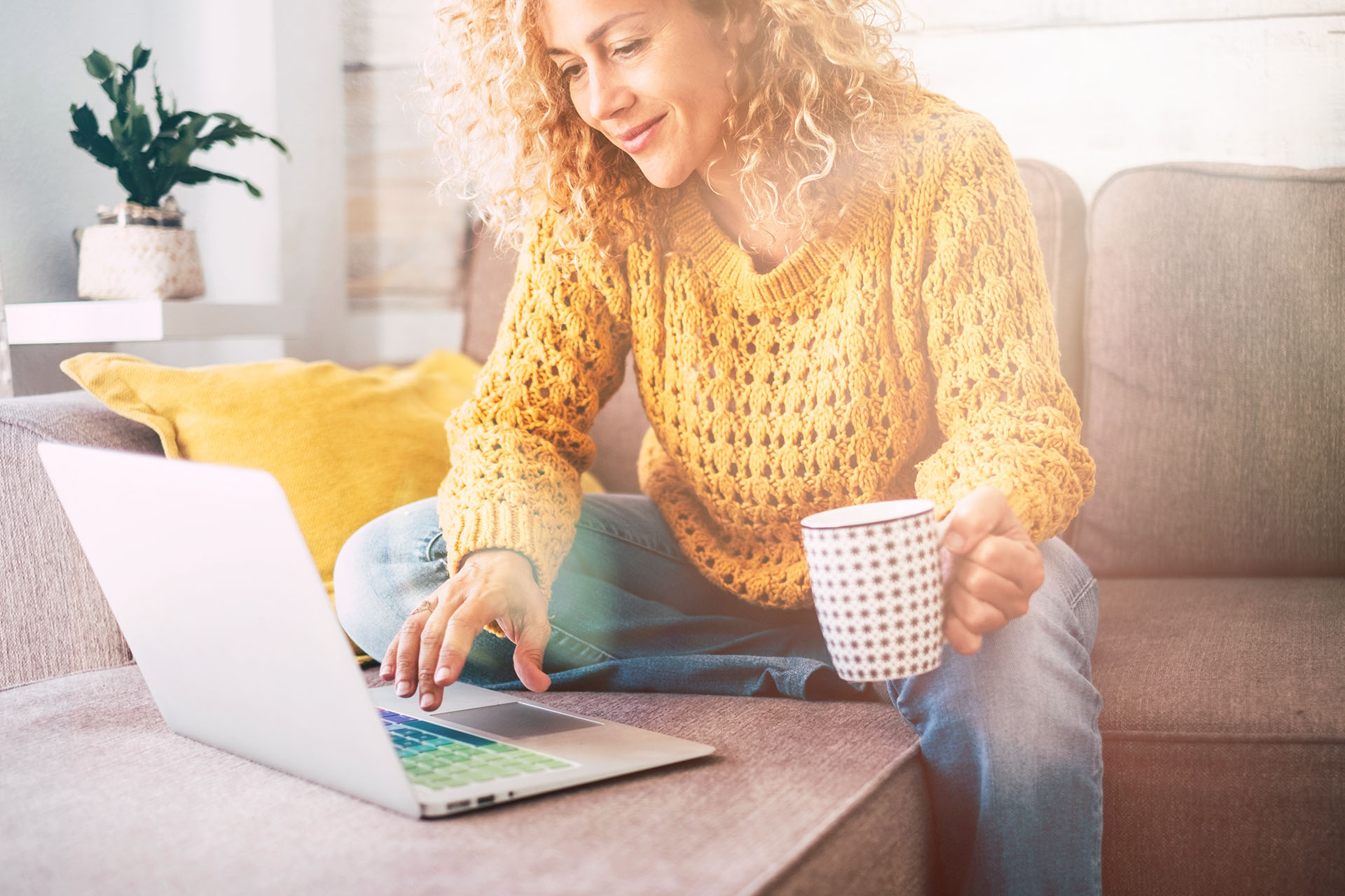Frau mit Tasse Kaffee sitzt auf Sofa und schaut auf Laptop